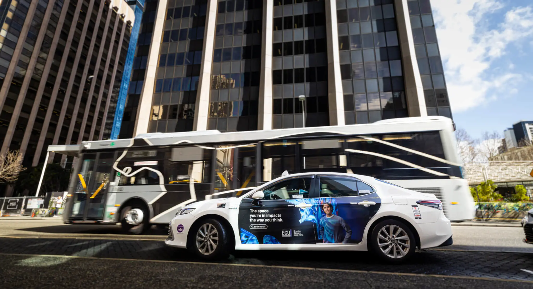 Taxi advertising on an Edith Cowan University branded taxi driving through Perth CBD with a bus passing in the background.