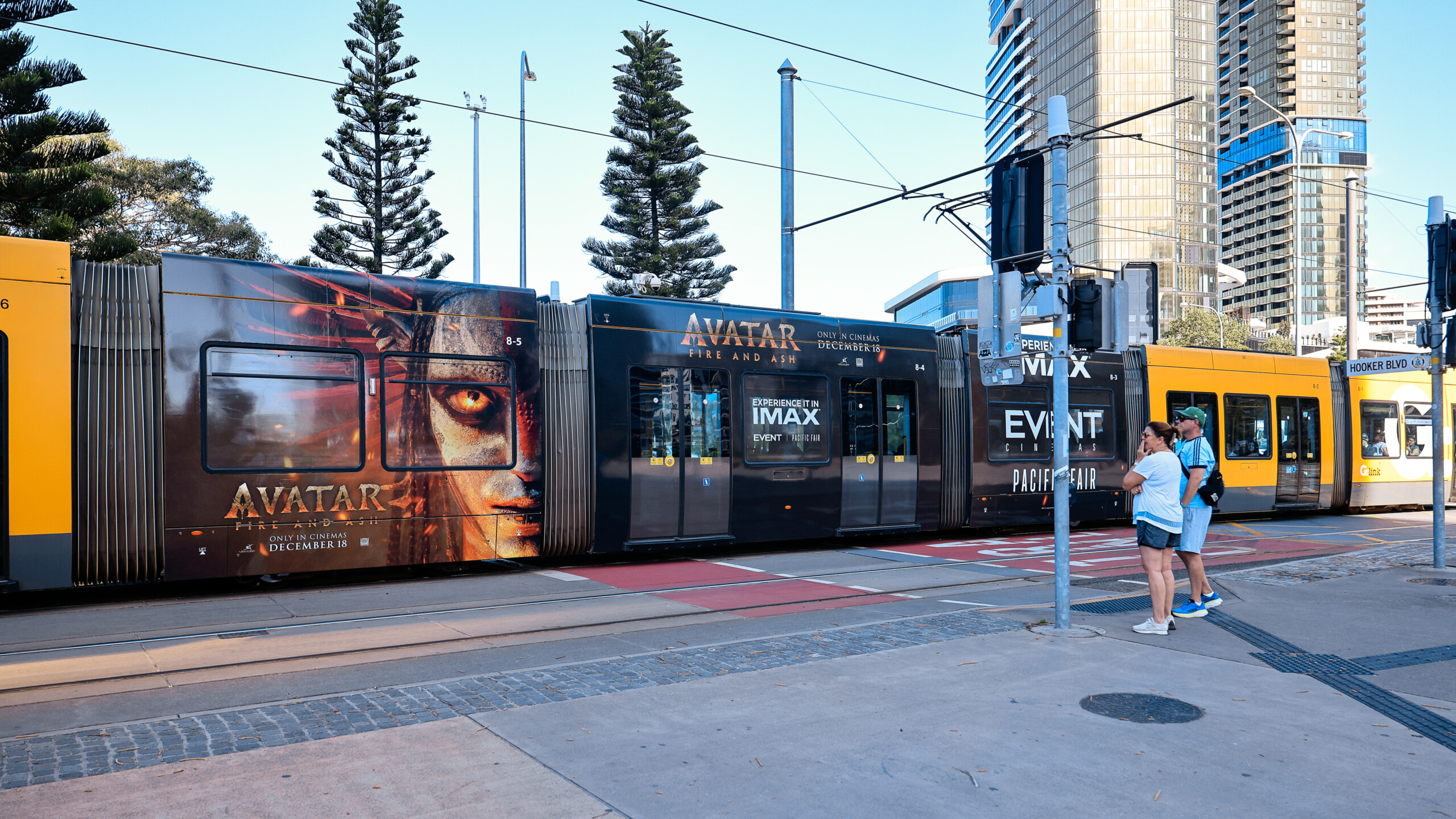 Light rail advertising featuring a full wrap for the Avatar: Fire and Ash movie on a Gold Coast tram, with pedestrians waiting at the station.