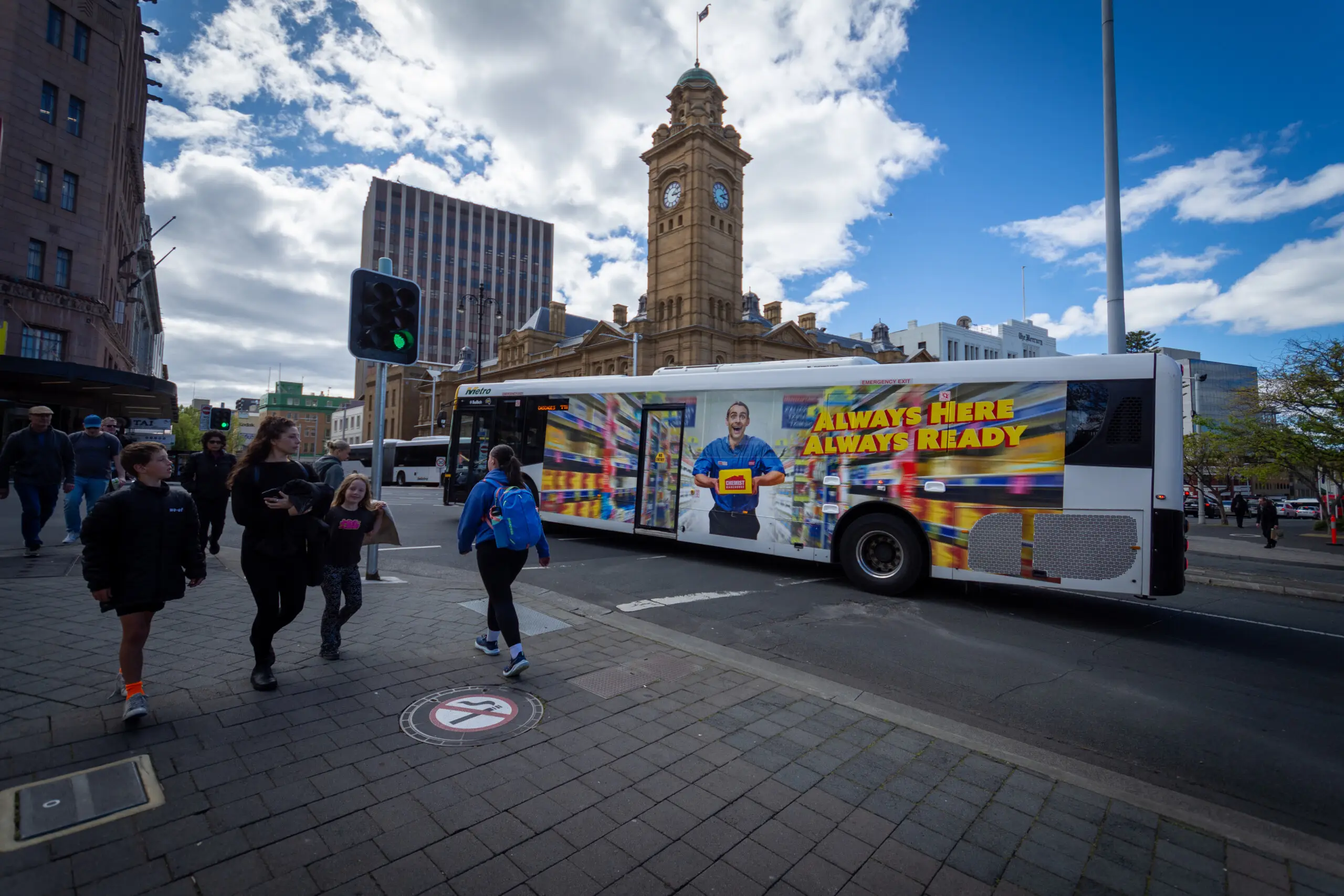 Bus advertising campaign for Chemist Warehouse travelling through Hobart CBD with pedestrians and the historic General Post Office clock tower in the background.