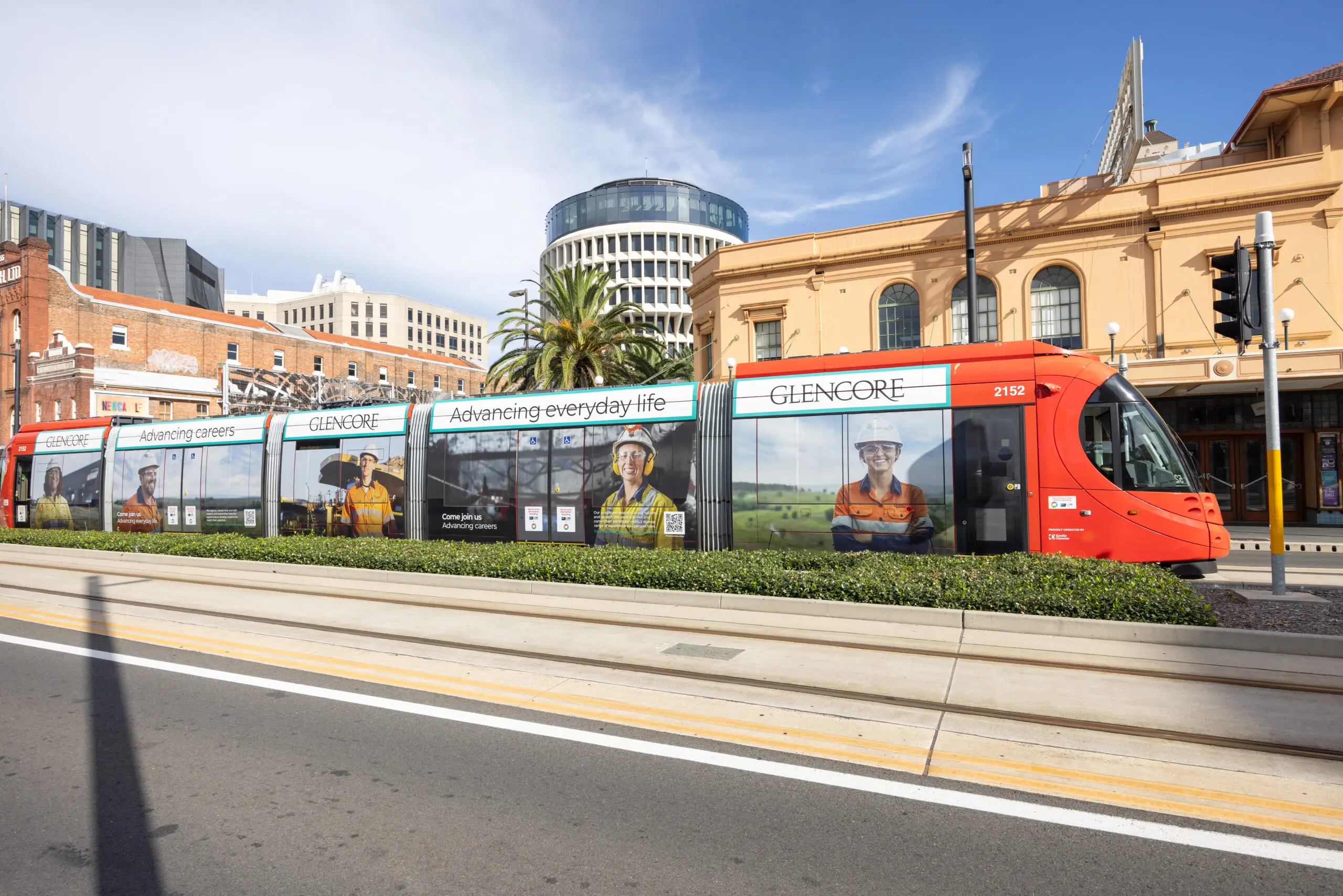Light rail premium transit advertising featuring a full Glencore wrap on a Newcastle tram travelling past historic city buildings in bright daylight.