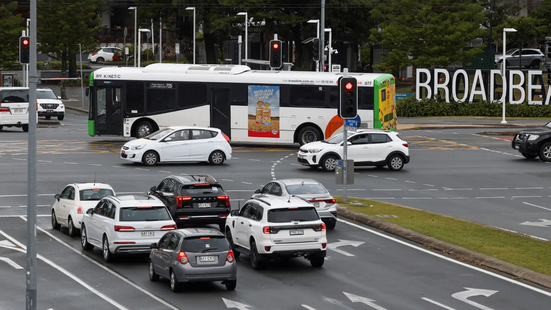 A TransLink bus with a bright advertisement for Sunblest bread drives through a busy city intersection near Broadbeach. The ad reads 