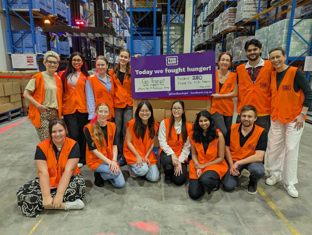 Volunteers from GoTransit, Zenith and Audience Group in orange vests at Foodbank Queensland, holding a sign reading “Today we fought hunger—packed 280 Food for Kids hampers.
