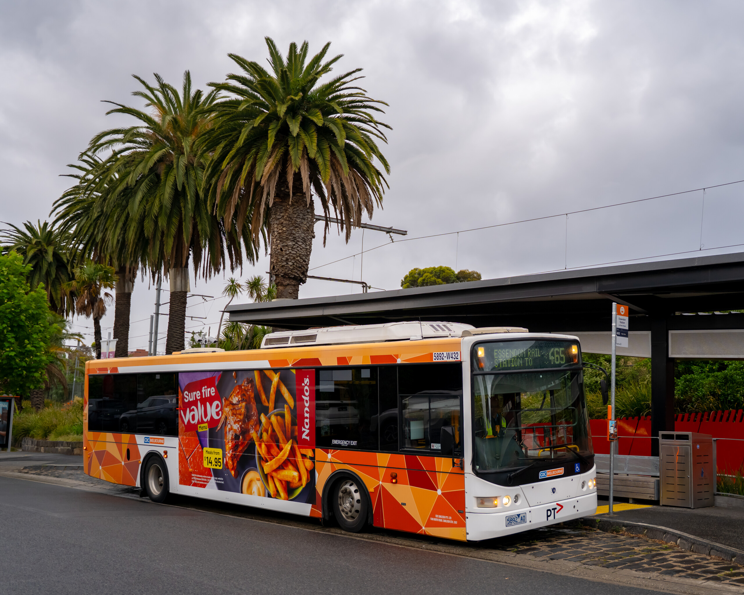 Side panel bus advertising featuring a Nando’s meal deal on a Melbourne bus pulling into a suburban station surrounded by palm trees.
