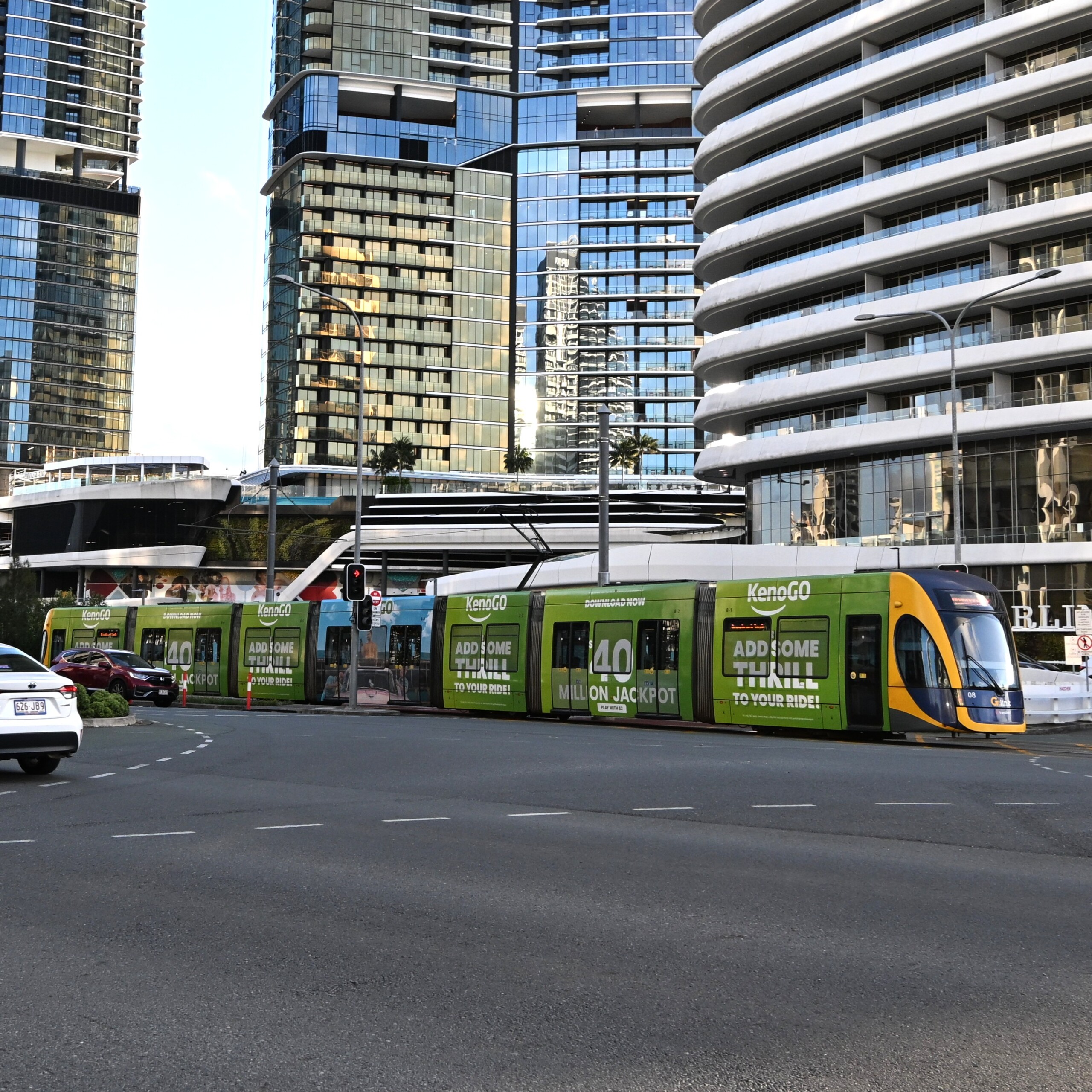 Light rail full wrap promoting KenoGO on a Gold Coast tram travelling through a modern city precinct with high-rise buildings.