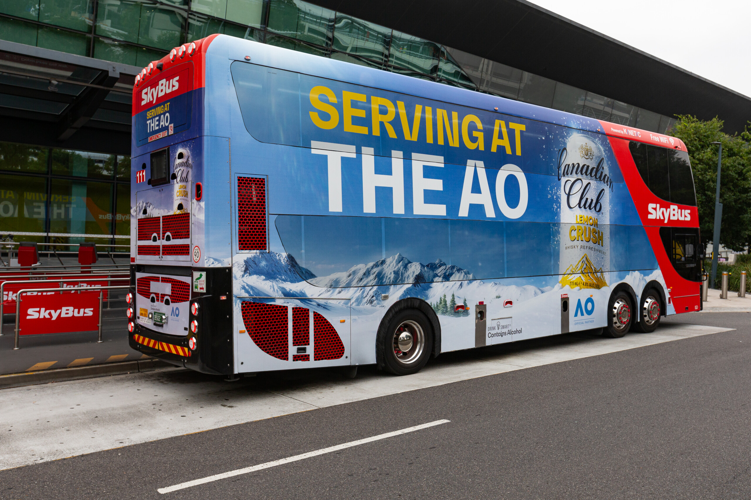 SkyBus double decker featuring large-format SkyBus advertising outside Melbourne Airport terminal.